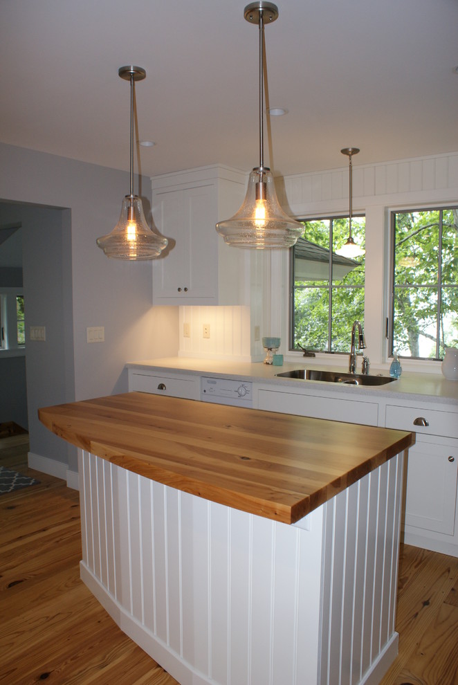 Foto på ett litet maritimt kök, med en undermonterad diskho, luckor med infälld panel, vita skåp, laminatbänkskiva, vitt stänkskydd, vita vitvaror, ljust trägolv och en köksö