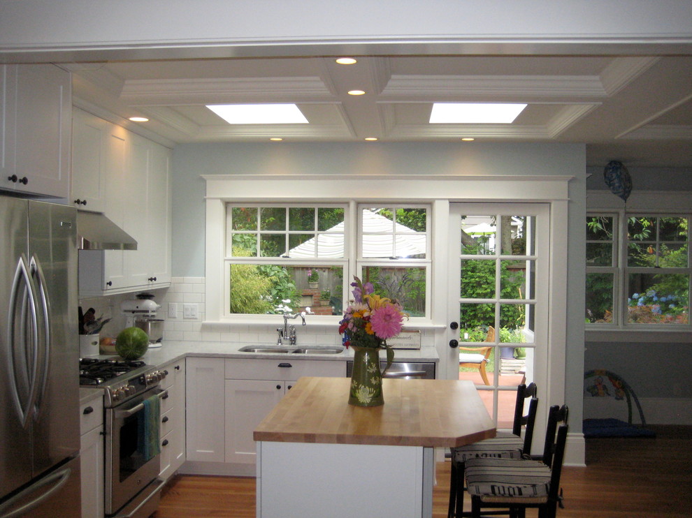 Inredning av ett klassiskt litet grå grått kök, med skåp i shakerstil, vita skåp, en köksö, en dubbel diskho, vitt stänkskydd, stänkskydd i keramik, rostfria vitvaror, mellanmörkt trägolv och brunt golv