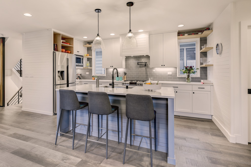 Photo of a small classic l-shaped open plan kitchen in Seattle with a submerged sink, shaker cabinets, white cabinets, engineered stone countertops, grey splashback, ceramic splashback, stainless steel appliances, medium hardwood flooring, an island, white worktops and grey floors.