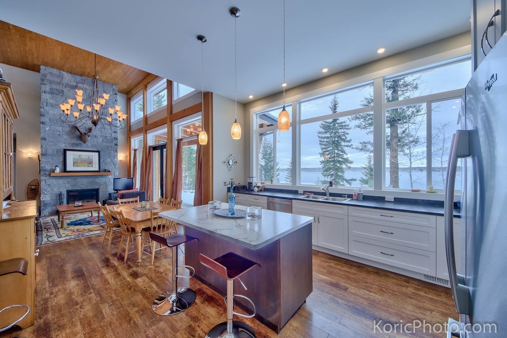 Mittelgroße Moderne Wohnküche in L-Form mit Doppelwaschbecken, weißen Schränken, Küchengeräten aus Edelstahl, braunem Holzboden und Kücheninsel in Vancouver