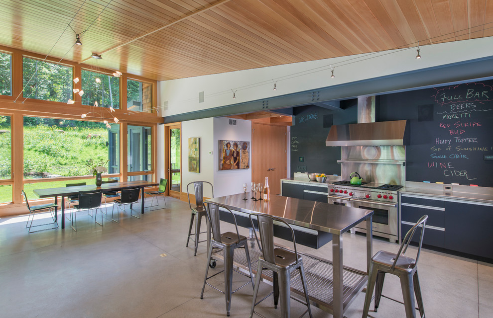 Bild på ett mellanstort funkis linjärt kök med öppen planlösning, med släta luckor, svarta skåp, bänkskiva i rostfritt stål, betonggolv, en köksö, en undermonterad diskho, grått stänkskydd, stänkskydd i metallkakel och rostfria vitvaror