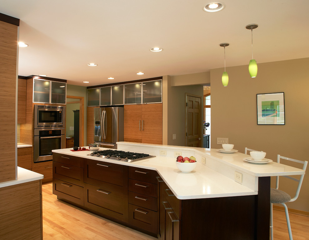 Photo of a contemporary l-shaped kitchen/diner in Milwaukee with a submerged sink, flat-panel cabinets, medium wood cabinets, glass tiled splashback and stainless steel appliances.