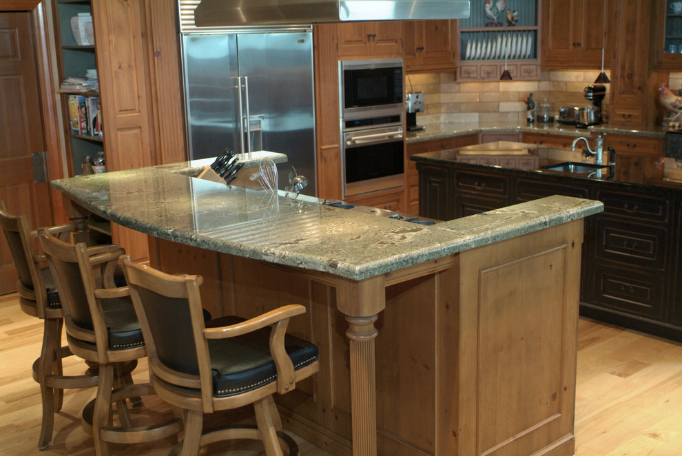 Example of a mountain style eat-in kitchen design in Seattle with a farmhouse sink, raised-panel cabinets, light wood cabinets, granite countertops, beige backsplash and black appliances