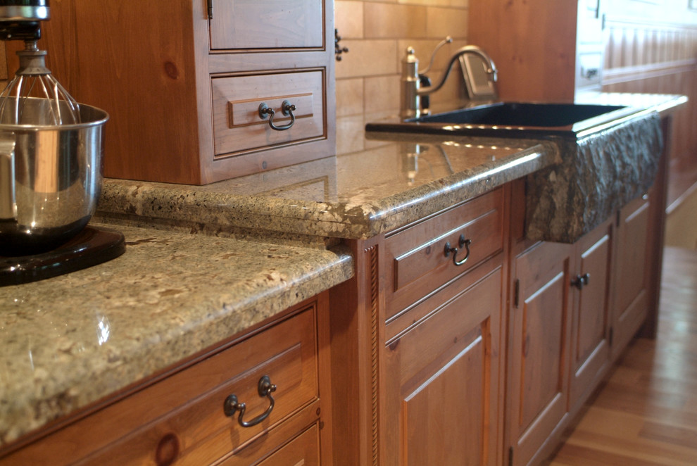 Immagine di una cucina abitabile rustica con lavello stile country, ante con bugna sagomata, ante in legno chiaro, top in granito, paraspruzzi beige e elettrodomestici neri