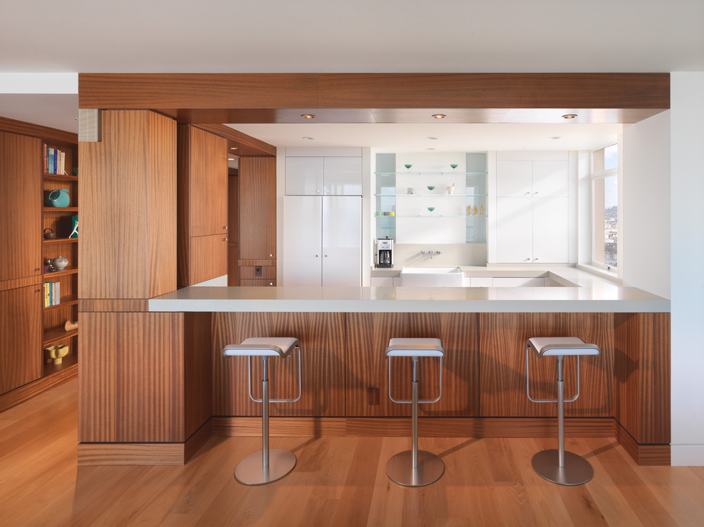 Inspiration for a medium sized contemporary u-shaped kitchen/diner in San Francisco with a belfast sink, flat-panel cabinets, white cabinets, white appliances, medium hardwood flooring, a breakfast bar and brown floors.