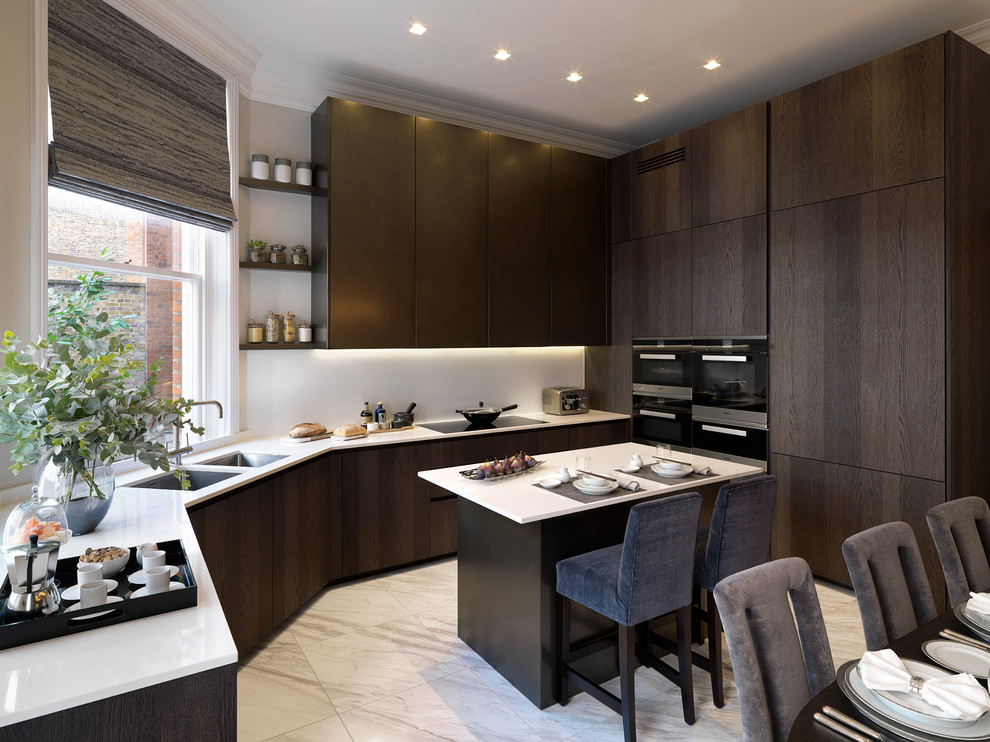 Trendy l-shaped open concept kitchen photo in London with a double-bowl sink, flat-panel cabinets, dark wood cabinets, gray backsplash, black appliances and an island