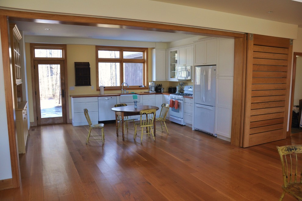 Example of a huge tuscan l-shaped light wood floor eat-in kitchen design in Bridgeport with a farmhouse sink, recessed-panel cabinets, white cabinets, wood countertops, yellow backsplash and white appliances
