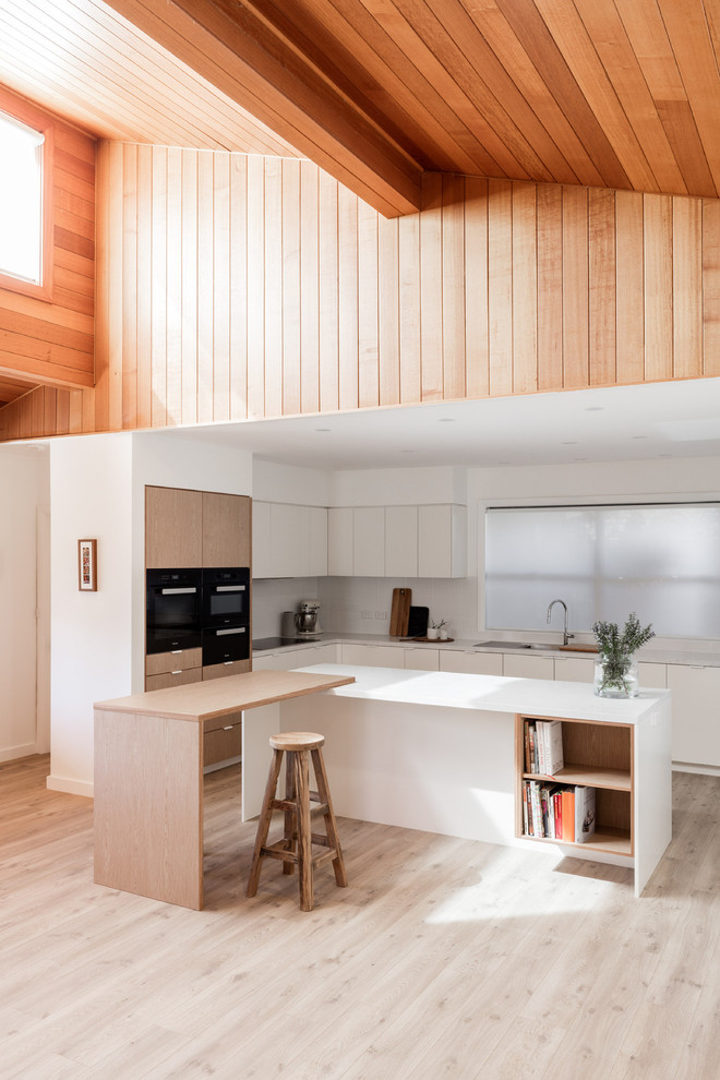 Источник вдохновения для домашнего уюта: угловая кухня-гостиная в современном стиле с двойной мойкой, плоскими фасадами, белыми фасадами, черной техникой, светлым паркетным полом и двумя и более островами