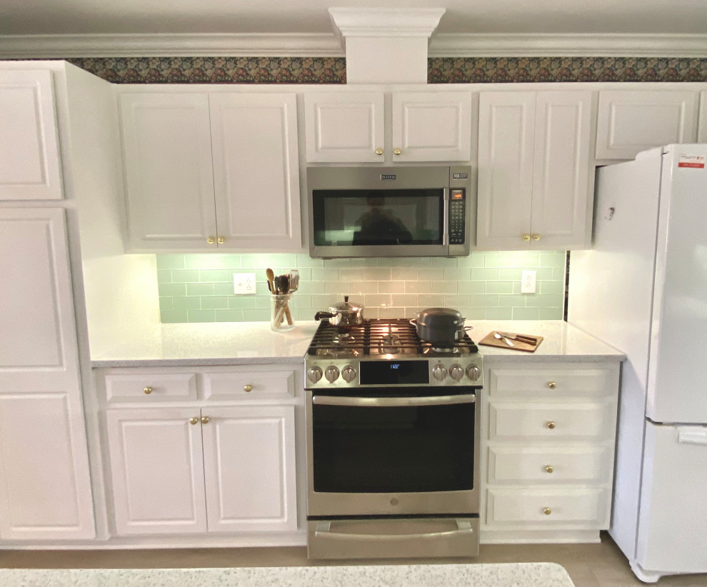 Foto på ett avskilt, mellanstort lantligt vit kök, med en undermonterad diskho, luckor med upphöjd panel, vita skåp, bänkskiva i kvarts, grönt stänkskydd, stänkskydd i glaskakel, rostfria vitvaror, vinylgolv, en köksö och brunt golv