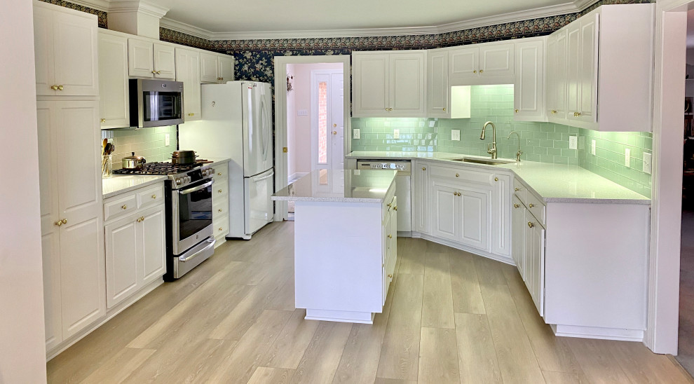 Lantlig inredning av ett avskilt, mellanstort vit vitt kök, med en undermonterad diskho, luckor med upphöjd panel, vita skåp, bänkskiva i kvarts, grönt stänkskydd, stänkskydd i glaskakel, rostfria vitvaror, vinylgolv, en köksö och brunt golv