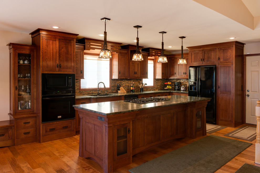 Inredning av ett amerikanskt mellanstort l-kök, med en undermonterad diskho, skåp i shakerstil, skåp i mellenmörkt trä, granitbänkskiva, flerfärgad stänkskydd, stänkskydd i stickkakel, svarta vitvaror, mellanmörkt trägolv, en köksö och brunt golv
