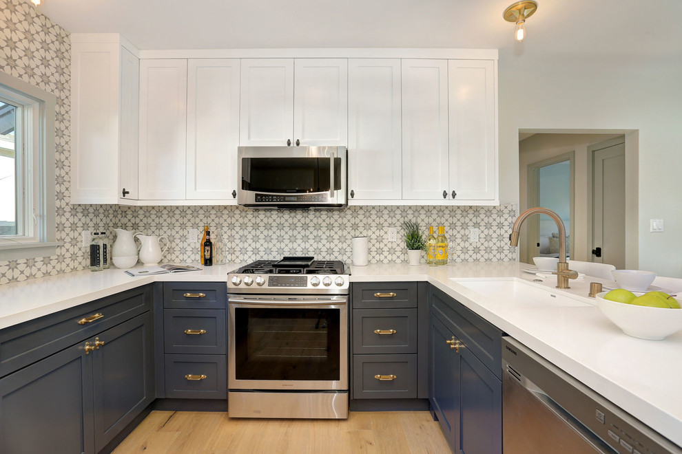 This is an example of a small traditional u-shaped kitchen/diner in Los Angeles with a submerged sink, shaker cabinets, engineered stone countertops, multi-coloured splashback, cement tile splashback, stainless steel appliances, light hardwood flooring, a breakfast bar, brown floors and blue cabinets.