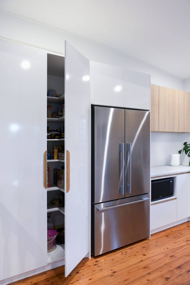 シドニーにあるお手頃価格の広い北欧スタイルのおしゃれなキッチン (ドロップインシンク、フラットパネル扉のキャビネット、白いキャビネット、ラミネートカウンター、白いキッチンパネル、セラミックタイルのキッチンパネル、シルバーの調理設備、無垢フローリング、茶色い床、グレーのキッチンカウンター) の写真