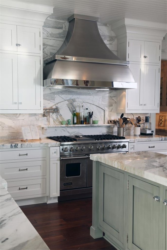 Klassisk inredning av ett kök, med en rustik diskho, skåp i shakerstil, vita skåp, vitt stänkskydd, rostfria vitvaror, mörkt trägolv och en köksö