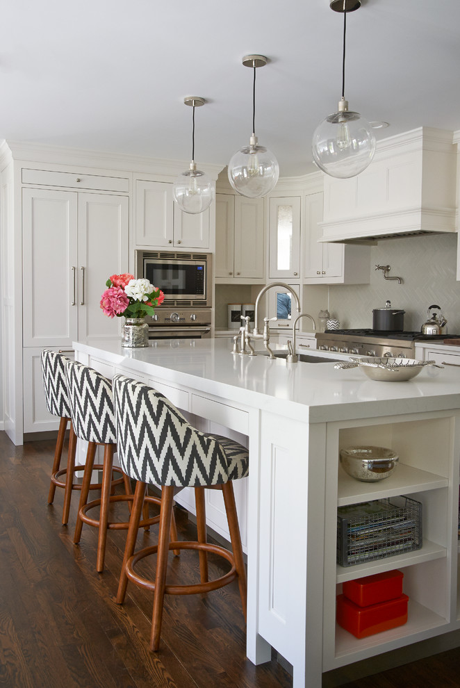 This is an example of a medium sized traditional l-shaped kitchen/diner in New York with shaker cabinets, white cabinets, engineered stone countertops, grey splashback, ceramic splashback, integrated appliances, dark hardwood flooring and an island.