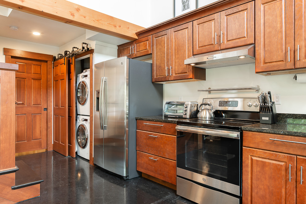 Photo of a traditional single-wall kitchen/diner in Seattle with a submerged sink, raised-panel cabinets, medium wood cabinets, granite worktops, black splashback, stone slab splashback, stainless steel appliances, concrete flooring, black floors and black worktops.