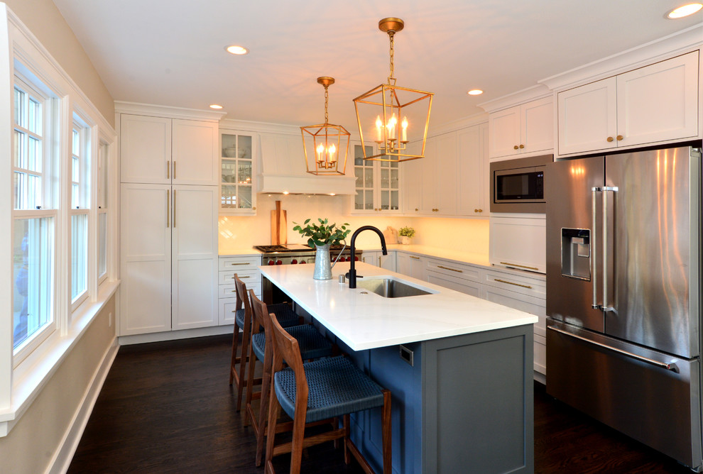 This is an example of a medium sized classic l-shaped open plan kitchen in Seattle with a submerged sink, shaker cabinets, white cabinets, engineered stone countertops, white splashback, ceramic splashback, stainless steel appliances, dark hardwood flooring, an island, brown floors and white worktops.