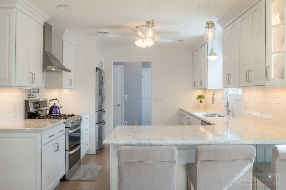Photo of a large galley kitchen/diner in New York with a submerged sink, raised-panel cabinets, white cabinets, engineered stone countertops, white splashback, ceramic splashback, stainless steel appliances, plywood flooring and a breakfast bar.