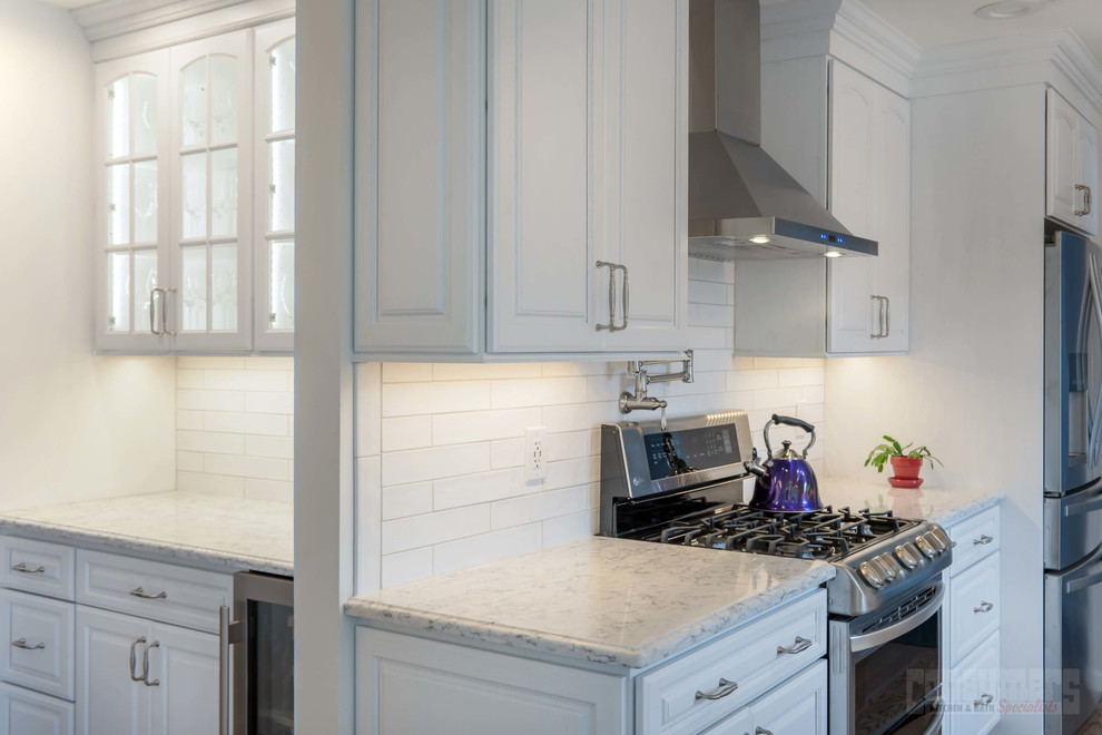 Example of a large galley plywood floor eat-in kitchen design in New York with an undermount sink, raised-panel cabinets, white cabinets, quartz countertops, white backsplash, ceramic backsplash, stainless steel appliances and a peninsula