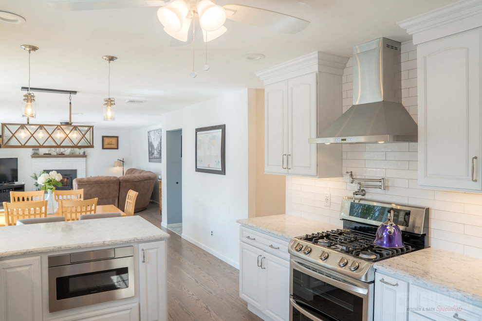 Large galley plywood floor eat-in kitchen photo in New York with an undermount sink, raised-panel cabinets, white cabinets, quartz countertops, white backsplash, ceramic backsplash, stainless steel appliances and a peninsula