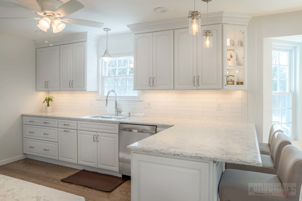 Foto på ett stort kök, med en undermonterad diskho, luckor med upphöjd panel, vita skåp, bänkskiva i kvarts, vitt stänkskydd, stänkskydd i keramik, rostfria vitvaror, plywoodgolv och en halv köksö