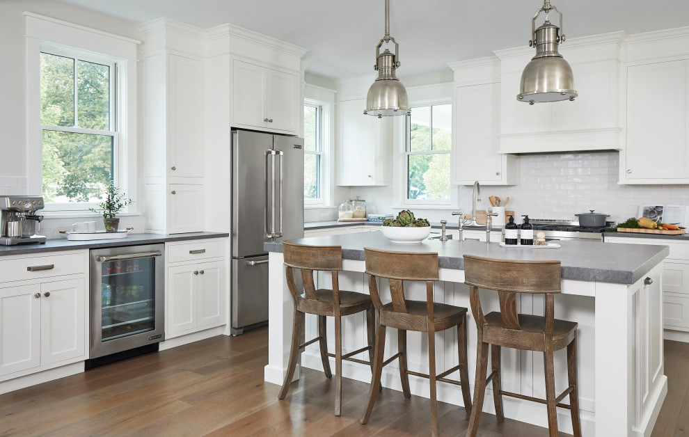 Medium sized farmhouse l-shaped open plan kitchen in Grand Rapids with a belfast sink, recessed-panel cabinets, white cabinets, concrete worktops, white splashback, metro tiled splashback, stainless steel appliances, medium hardwood flooring, an island and grey worktops.