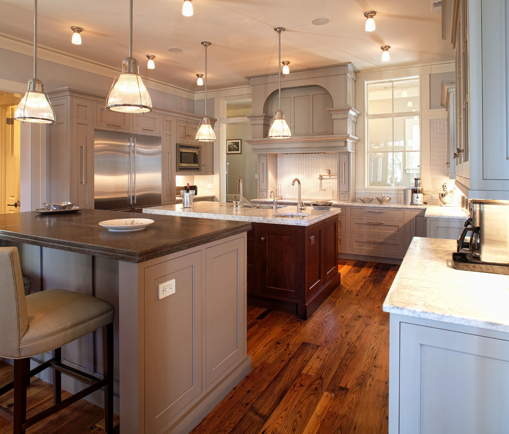 Klassisk inredning av ett stort kök, med en undermonterad diskho, luckor med infälld panel, grå skåp, granitbänkskiva, grått stänkskydd, stänkskydd i keramik, rostfria vitvaror, mellanmörkt trägolv och flera köksöar