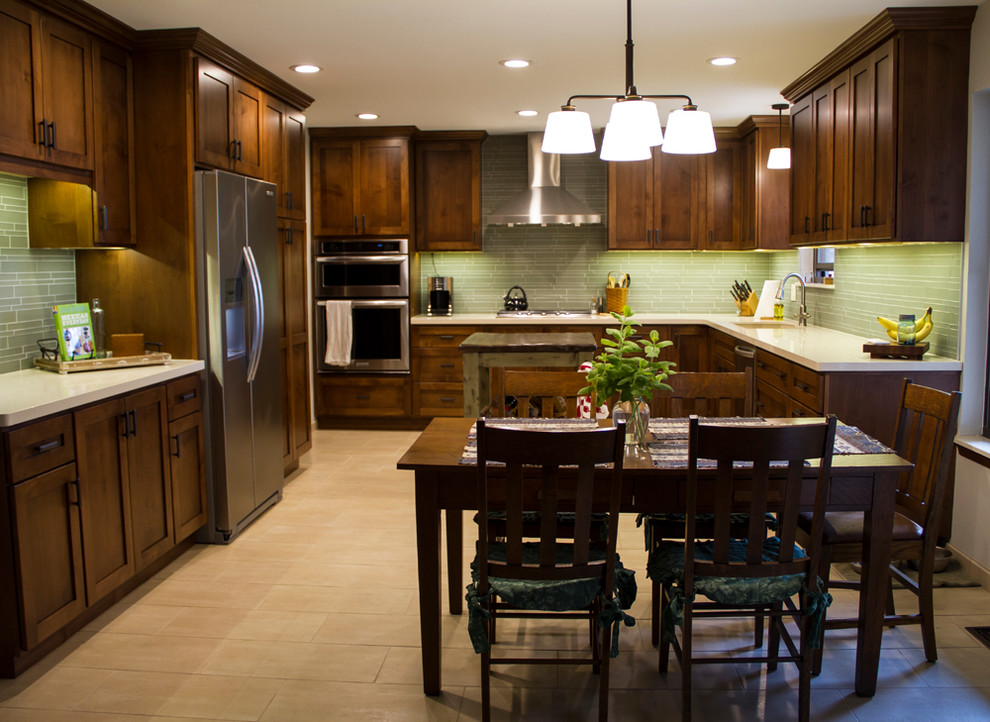 This is an example of a medium sized classic kitchen/diner in Oklahoma City with a submerged sink, flat-panel cabinets, medium wood cabinets, engineered stone countertops, green splashback, glass tiled splashback, stainless steel appliances, porcelain flooring and an island.