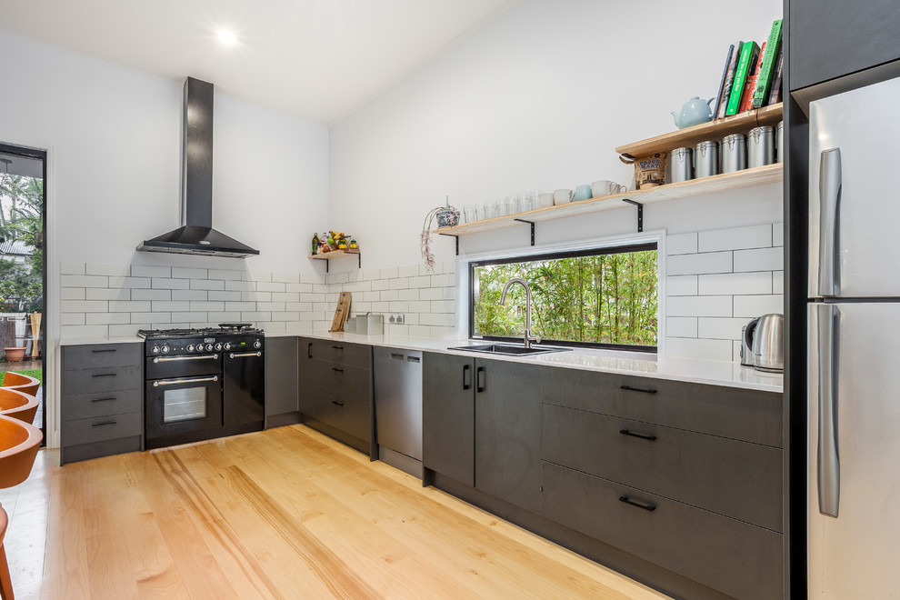 Moderne Wohnküche ohne Insel in L-Form mit Einbauwaschbecken, flächenbündigen Schrankfronten, Küchenrückwand in Weiß, Rückwand aus Metrofliesen, schwarzen Elektrogeräten und hellem Holzboden in Brisbane