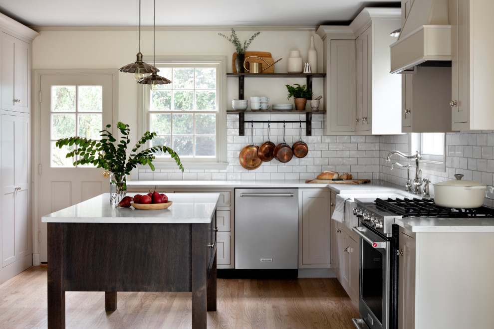 Mid-sized farmhouse l-shaped light wood floor kitchen photo in Baltimore with a farmhouse sink, shaker cabinets, quartz countertops, white backsplash, stainless steel appliances, an island, white countertops, gray cabinets and subway tile backsplash