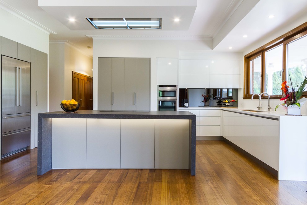 Design ideas for a large contemporary u-shaped kitchen/diner in Melbourne with a submerged sink, flat-panel cabinets, engineered stone countertops, mirror splashback, stainless steel appliances, medium hardwood flooring and an island.