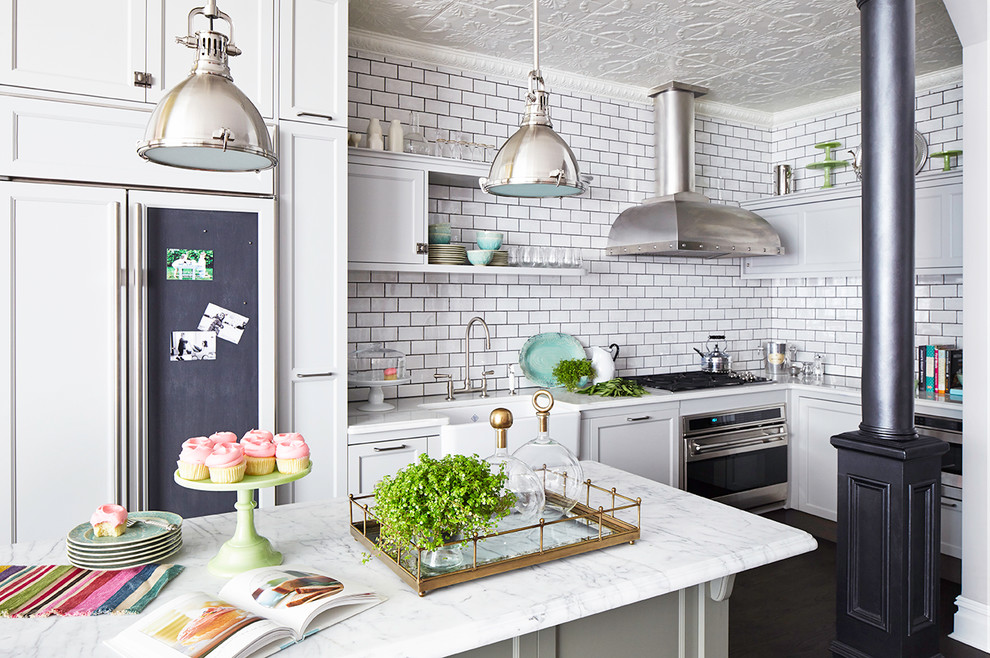 Elegant l-shaped kitchen photo in New York with a farmhouse sink, shaker cabinets, white cabinets, white backsplash, subway tile backsplash, paneled appliances and an island