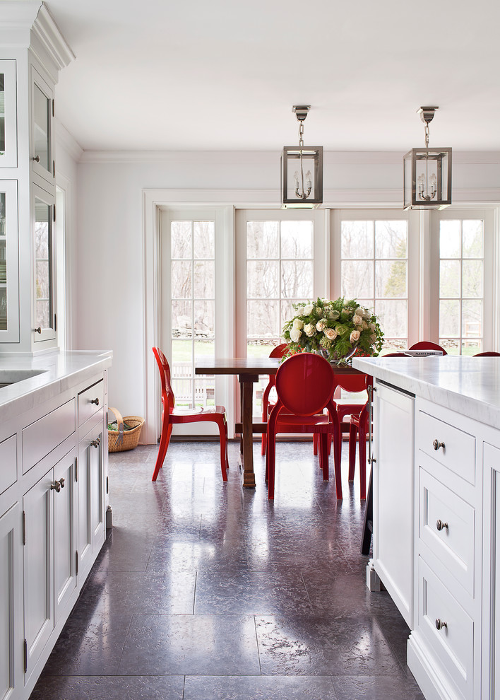 Klassisk inredning av ett stort kök, med en undermonterad diskho, luckor med profilerade fronter, vita skåp, marmorbänkskiva, stänkskydd i sten, vita vitvaror, kalkstensgolv och en köksö