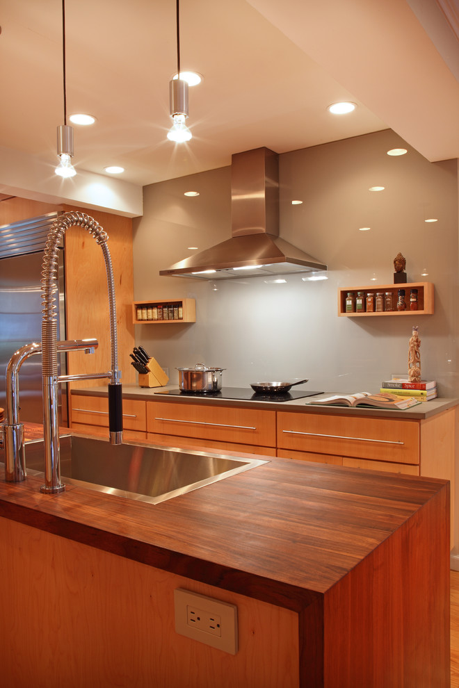 This is an example of a contemporary galley kitchen/diner in San Francisco with a submerged sink, flat-panel cabinets, light wood cabinets, limestone worktops, grey splashback, glass sheet splashback and stainless steel appliances.