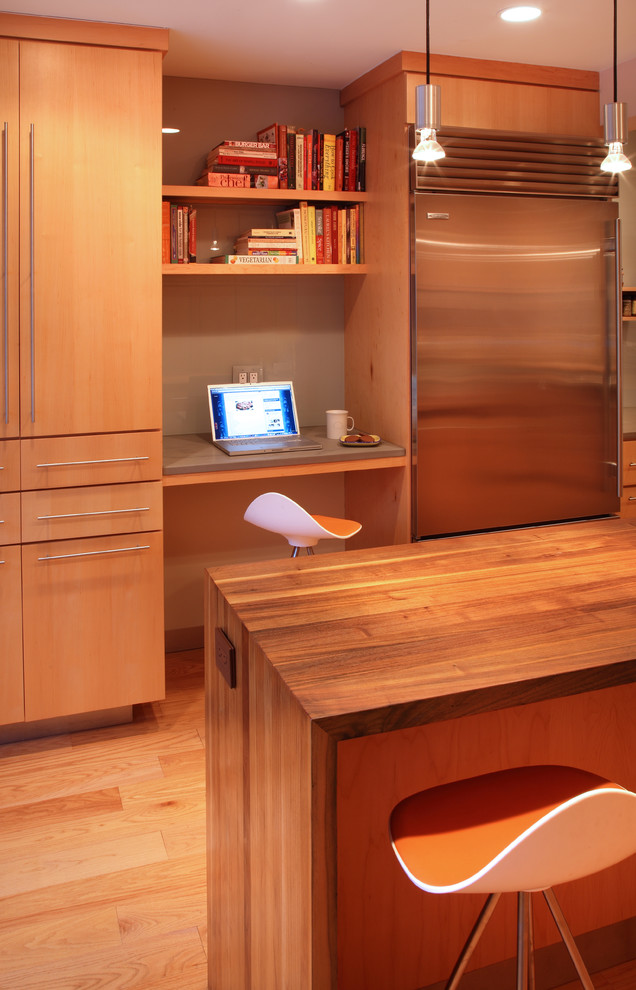 Cette image montre une cuisine américaine parallèle design en bois brun avec un placard à porte plane, un plan de travail en bois, une crédence grise, une crédence en feuille de verre et un électroménager en acier inoxydable.