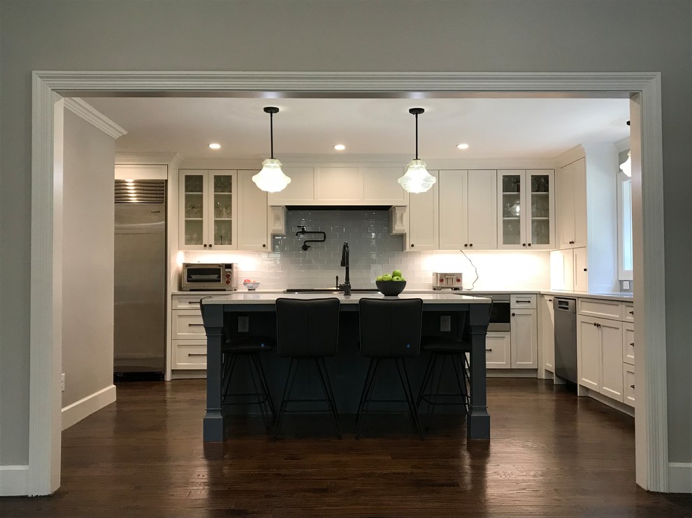 Inspiration for a traditional grey and cream kitchen in Dallas with a single-bowl sink, flat-panel cabinets, engineered stone countertops, grey splashback, glass tiled splashback, stainless steel appliances, dark hardwood flooring, brown floors and white worktops.