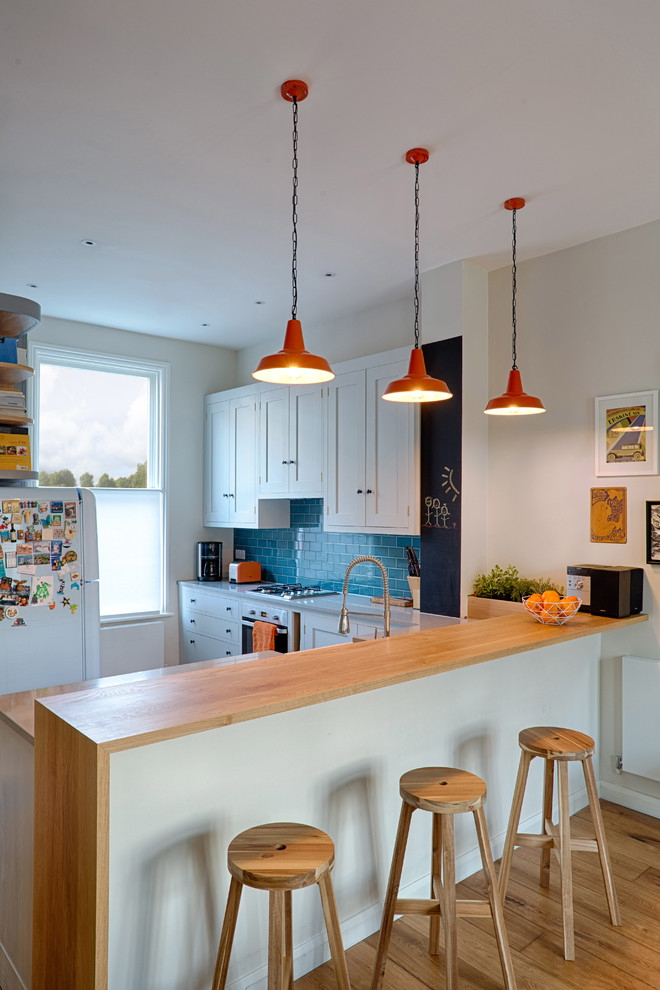 This is an example of a medium sized modern u-shaped open plan kitchen in Hampshire with a belfast sink, shaker cabinets, grey cabinets, composite countertops, blue splashback, metro tiled splashback, integrated appliances, porcelain flooring and a breakfast bar.