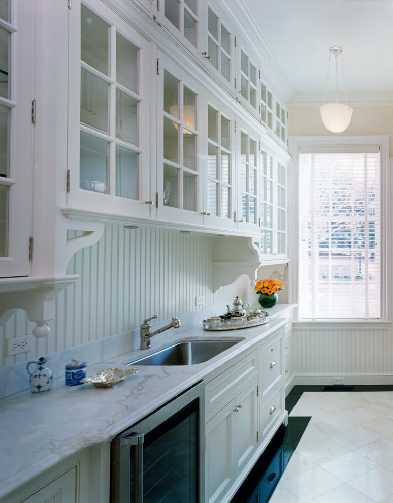 Bild på ett avskilt vintage kök, med en undermonterad diskho, luckor med glaspanel, vita skåp, vitt stänkskydd, stänkskydd i keramik, integrerade vitvaror, kalkstensgolv och en köksö