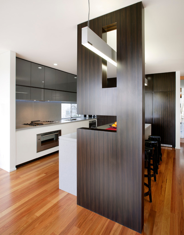 Design ideas for a medium sized contemporary l-shaped kitchen/diner in Sydney with a submerged sink, glass-front cabinets, engineered stone countertops, stone slab splashback, dark wood cabinets, grey splashback, stainless steel appliances, medium hardwood flooring and an island.