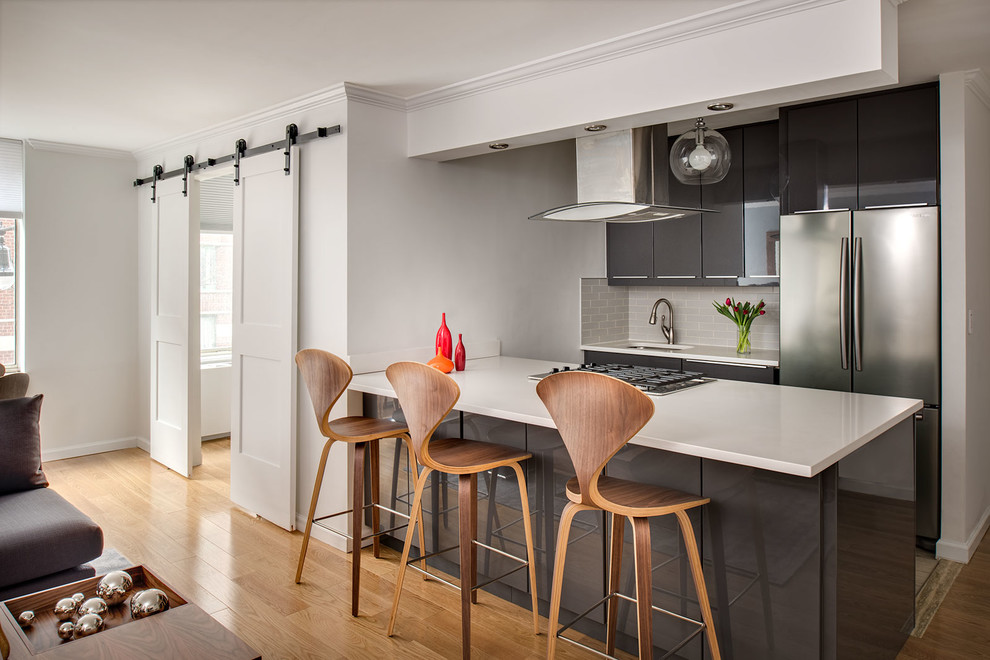 Пример оригинального дизайна: кухня-гостиная в современном стиле с врезной мойкой, плоскими фасадами, серым фартуком, фартуком из плитки кабанчик, техникой из нержавеющей стали, полуостровом и коричневыми фасадами