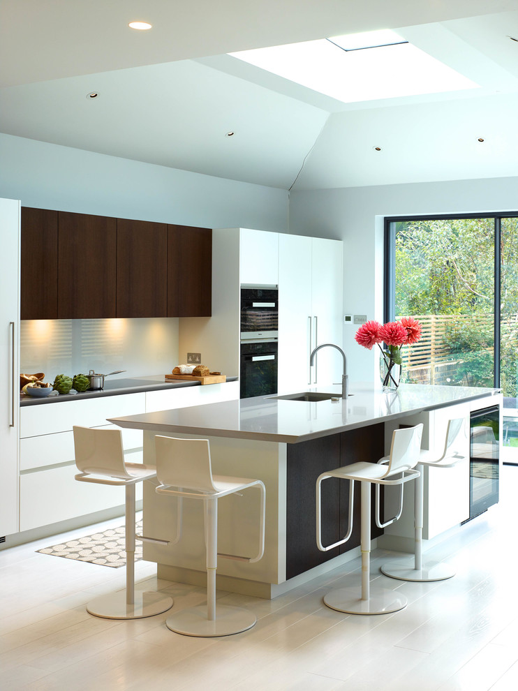 Large contemporary galley kitchen in London with a submerged sink, flat-panel cabinets, white cabinets, an island, white splashback, stainless steel appliances and ceramic flooring.
