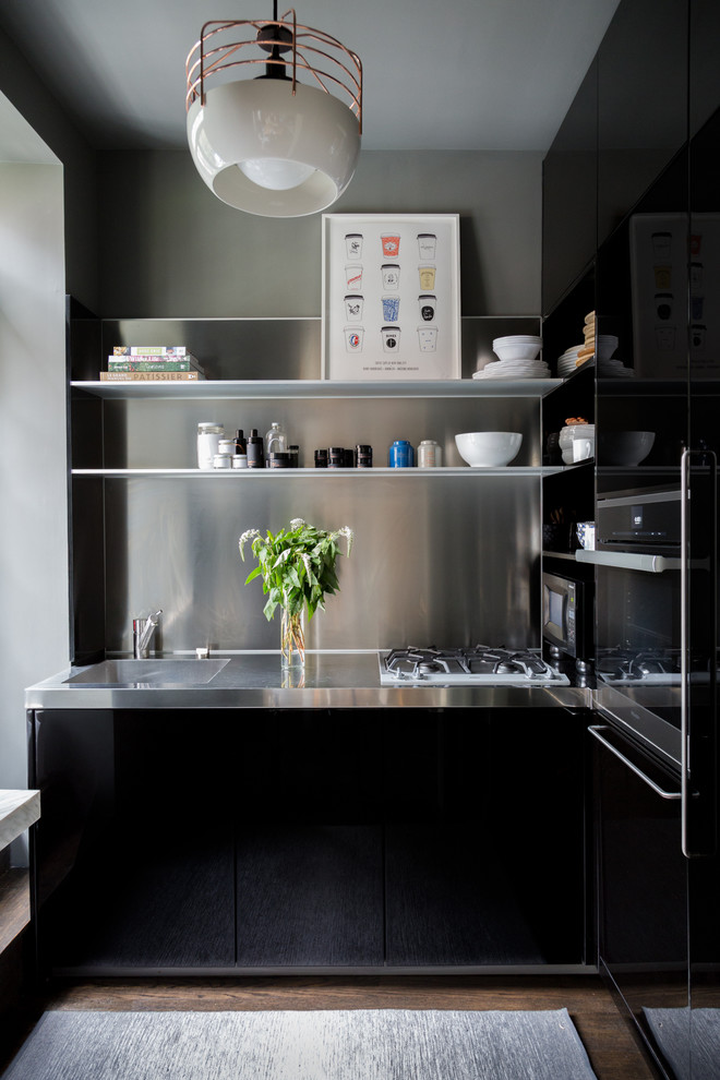Kleine Moderne Küche ohne Insel mit integriertem Waschbecken, flächenbündigen Schrankfronten, schwarzen Schränken, Edelstahl-Arbeitsplatte, Küchenrückwand in Metallic und dunklem Holzboden in New York
