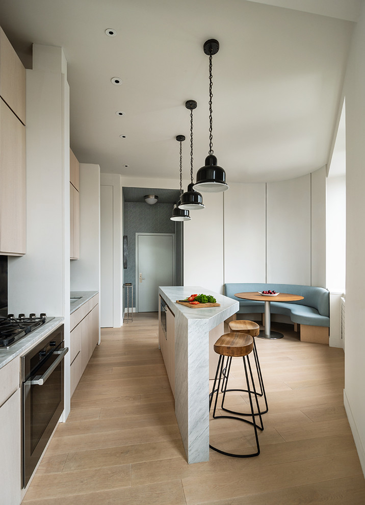 Photo of a contemporary galley kitchen in New York with a submerged sink, flat-panel cabinets, light wood cabinets, stainless steel appliances, medium hardwood flooring, an island, brown floors and white worktops.