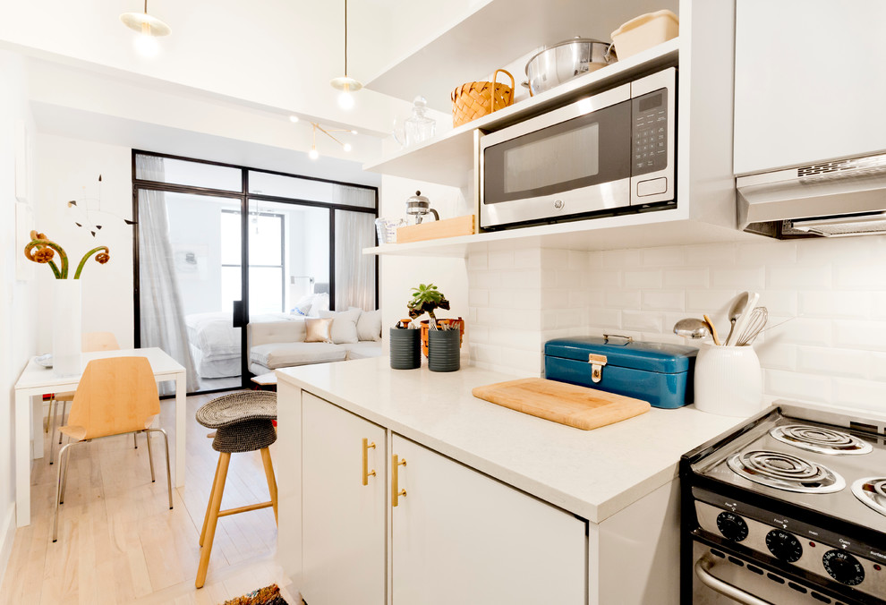 Small contemporary l-shaped open plan kitchen in New York with a submerged sink, open cabinets, white cabinets, engineered stone countertops, white splashback, metro tiled splashback, integrated appliances, light hardwood flooring and no island.