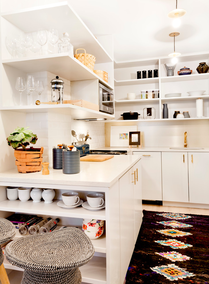 Modern inredning av ett litet kök, med en undermonterad diskho, öppna hyllor, vita skåp, vitt stänkskydd, integrerade vitvaror, ljust trägolv, bänkskiva i kvarts och stänkskydd i tunnelbanekakel