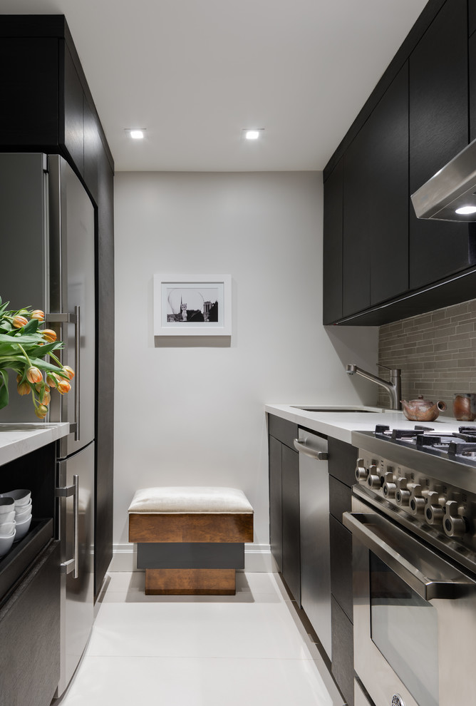 Inspiration for a classic galley kitchen in New York with a submerged sink, flat-panel cabinets, black cabinets, grey splashback, stainless steel appliances and white floors.