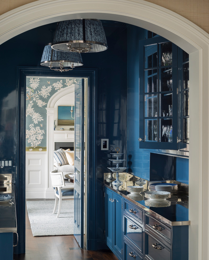 Cette photo montre une grande cuisine américaine parallèle chic avec un placard à porte vitrée, des portes de placard bleues, un plan de travail en inox, un électroménager en acier inoxydable, un sol en bois brun, un sol marron et une crédence bleue.