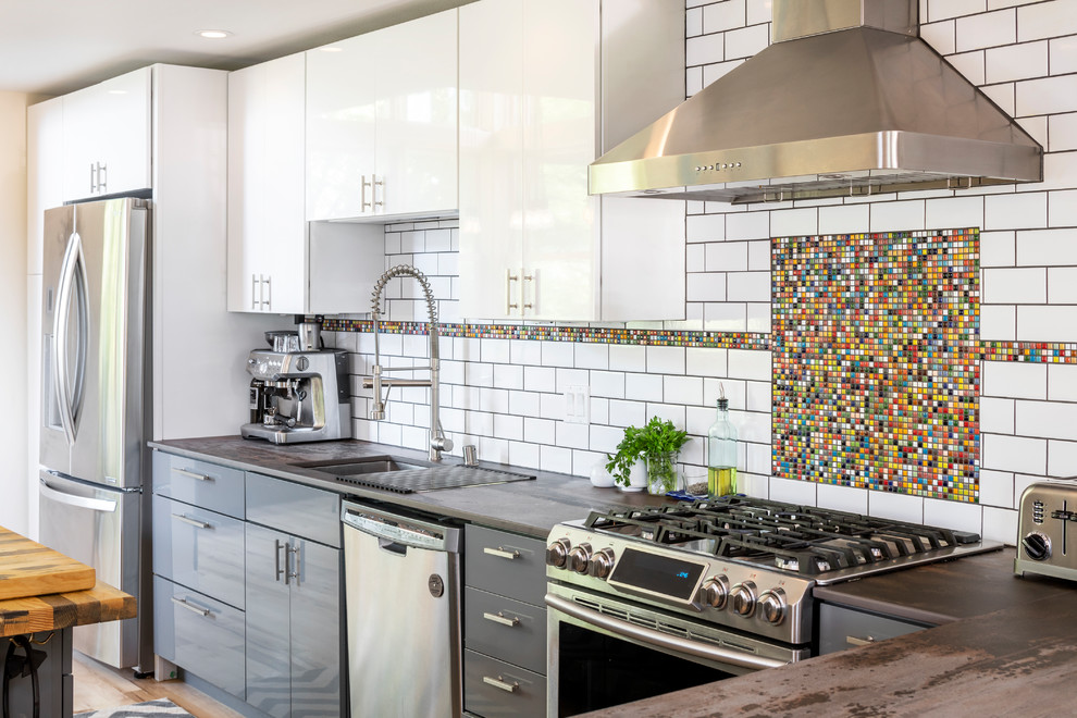 Inspiration for an industrial kitchen remodel in Seattle with an undermount sink, flat-panel cabinets, gray cabinets, multicolored backsplash, mosaic tile backsplash, stainless steel appliances and brown countertops