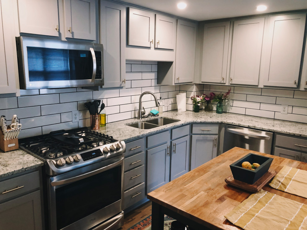 Foto på ett mellanstort lantligt grå kök, med en undermonterad diskho, skåp i shakerstil, grå skåp, granitbänkskiva, vitt stänkskydd, stänkskydd i keramik, rostfria vitvaror, vinylgolv, en köksö och brunt golv