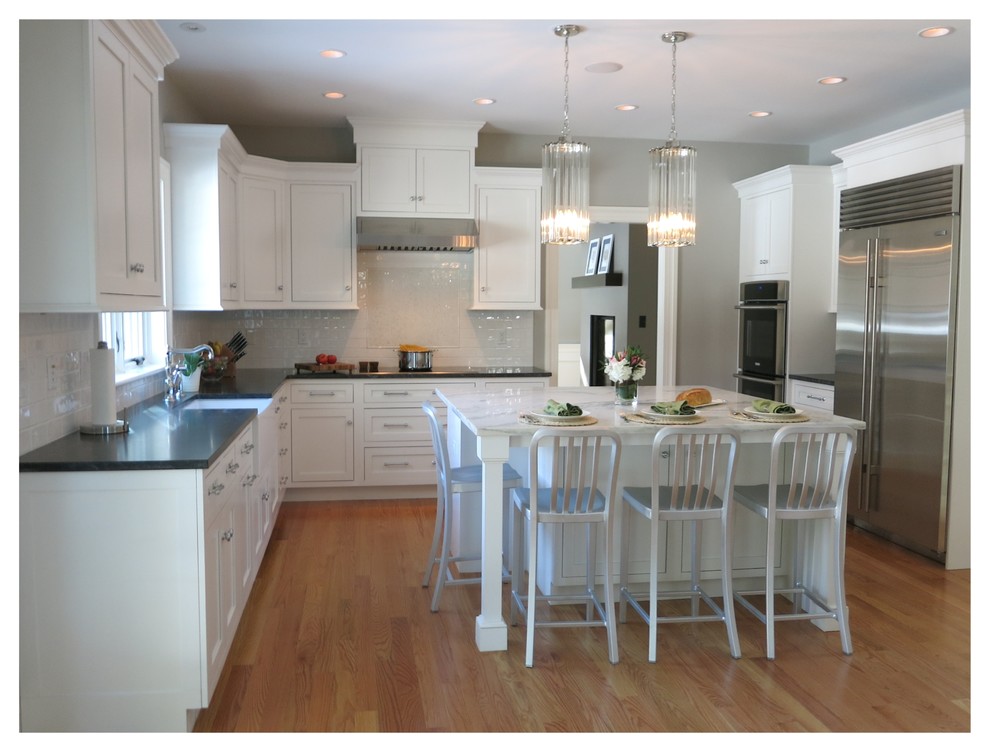 Mid-sized transitional u-shaped light wood floor and brown floor enclosed kitchen photo in Boston with shaker cabinets, an island, a farmhouse sink, stainless steel cabinets, soapstone countertops, white backsplash, subway tile backsplash and stainless steel appliances
